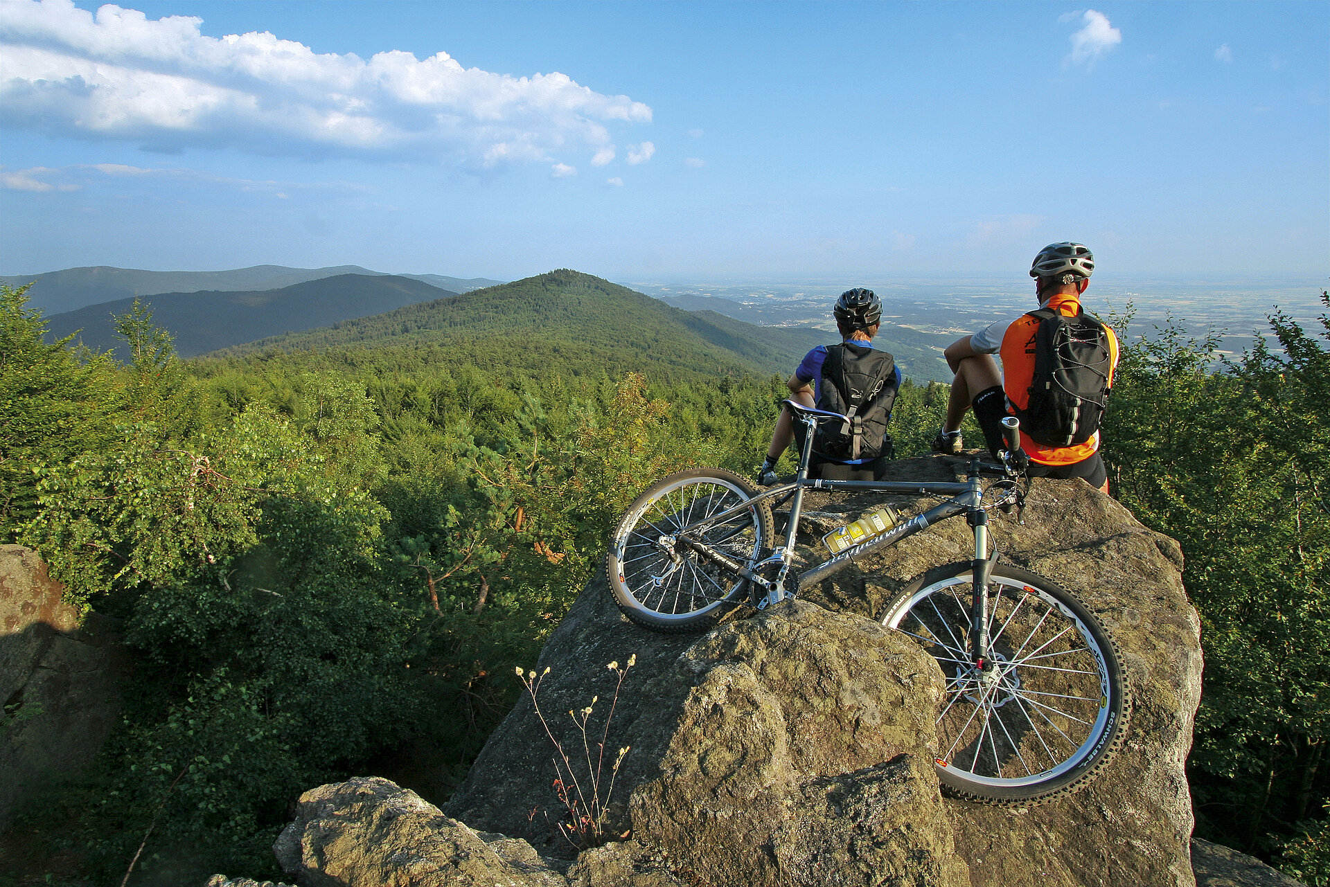 Zwei Mountainbiker sitzen auf einem Felsen und genießen einen einzigartigen Blick auf das Hirschensteingebiet. Das Mountainbike haben die Radlfahrer dahinter auf einem Felsen abgelegt.