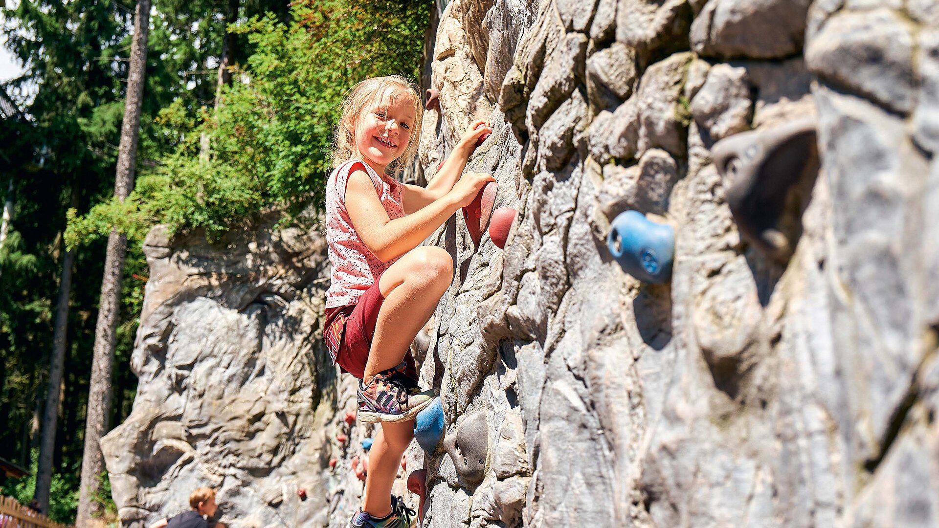 Kinder kraxeln voller Freude und Ehrgeiz an Kletterwand beim Waldwipfelweg
