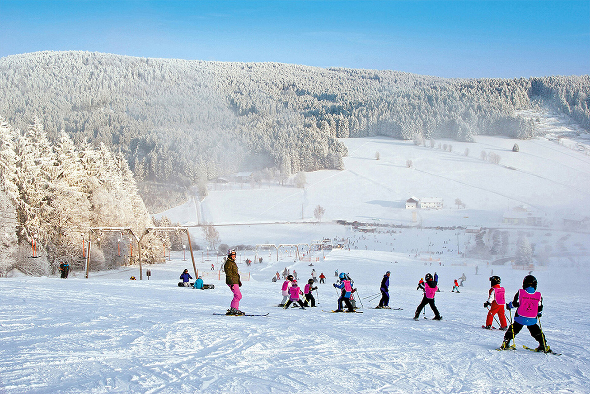 Skispass und Kinderskikurs am Skilift Grün-Maibrunn. Pulverschneepiste, schneebedeckte Landschaft und Bäume, blauer Himmel.
