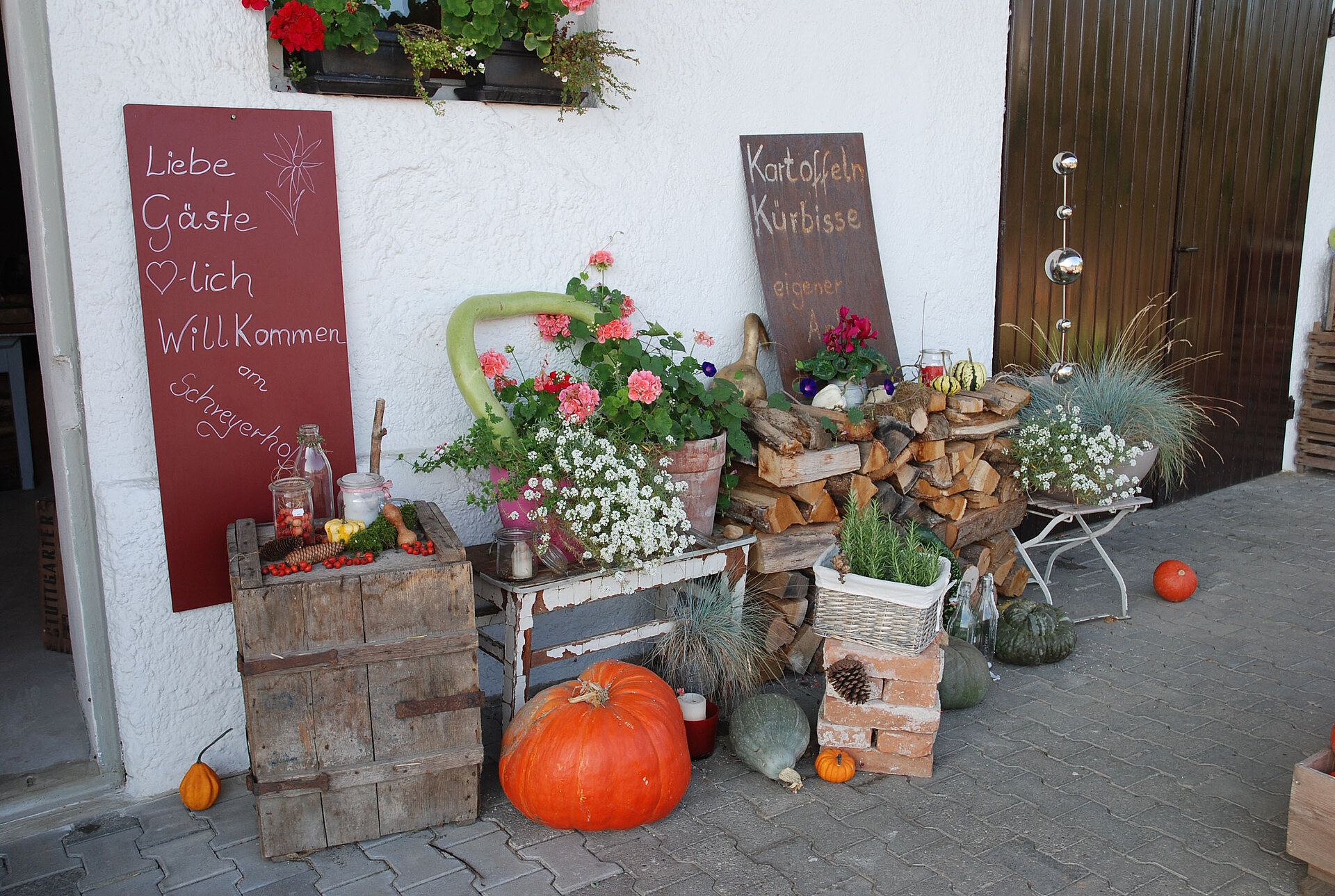 An der Hofmauer liegt ordentlich aufgeschichtetes Holz.  Kürbisse, Kräuter, Blumen und vieles mehr zieren den Eingang zum Hofladen der Familie Schreyer in Atting.